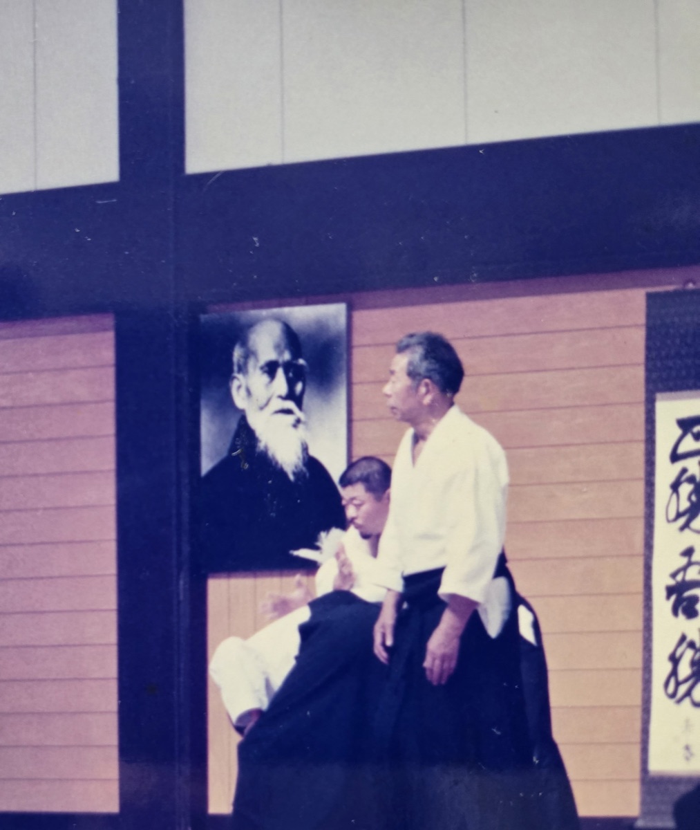 Morihiro Saito Shihan at the Iwama Dojo beneath a portrait of O-Sensei